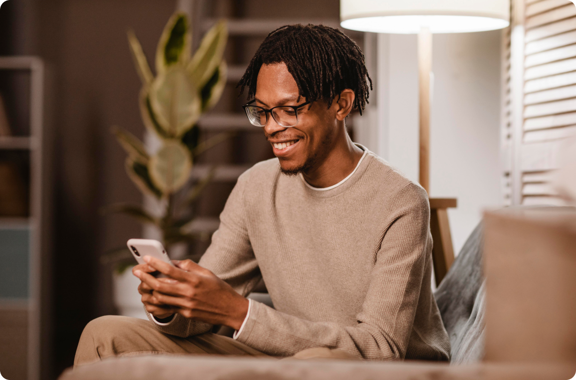 Homem negro sorrindo olhando celular vestindo moletom cinza